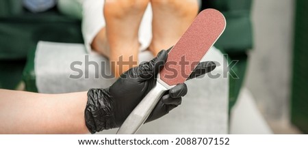 Special grater for scrubbing heels in hands of nail pedicure technician on feet background in beauty salon closeup