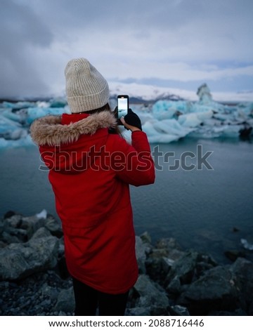 Woman standing by a frozen river, taking photo of ice field in Iceland, Europe. Taking photograph of beautiful Icelandic nature 