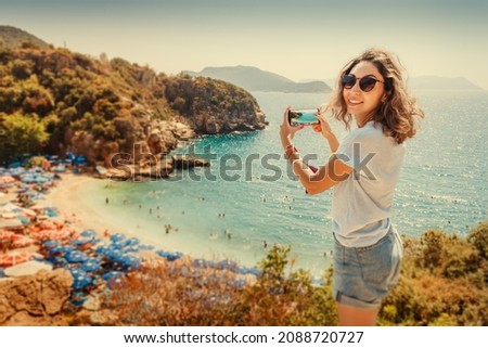 Tourist girl taking photos on smartphone of the scenic beach Buyukcakil in resort town of Kas in Turkey. Sightseeing and travel blogger concept
