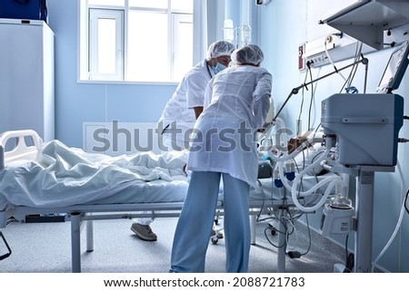 Two friendly doctors nurses help injured sick person, in hospital ward room. covid-19 patient with medical equipment, injected, under dropepr. on bed in hospital, coronavirus concept. Royalty-Free Stock Photo #2088721783