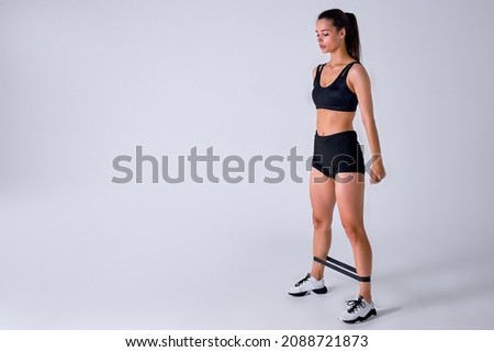caucasian sports fitness woman in sportswear working out with elastic band isolated on white studio background. Sport exercises, healthy lifestyle. Stretching legs, doing lunges. side view portrait