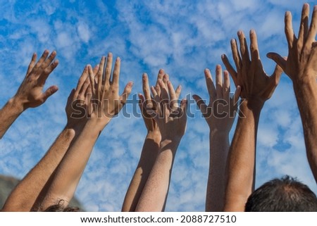 Group of people raise hands in air across blue sky with white clouds, close up