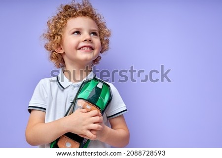 child boy holding green toy car in hands, having fun, excited, isolated on purple studio background. portrait of caucasian curly kid in casual wear dreaming about real car, looking up Royalty-Free Stock Photo #2088728593