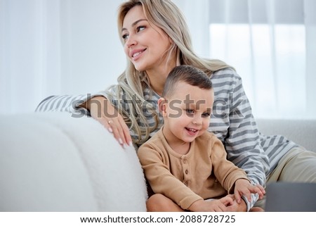 Carefree female parent have rest with preschooler son in living room wathcing cartoons, at home. Cheerful funny family mother and kid activity for indoor weekend or quarantine relax