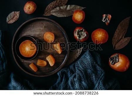 persimmon on a black background. pieces of persimmon on a wooden plate on a black table. autumn still life with persimmon and knitted scarf on a black table