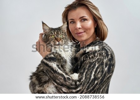 Smiling caucasian woman holding and hugging her furry Maine Coon cat. Concept of relationship between human and animal. Idea of owner and pet friendship. Isolated on white background in studio