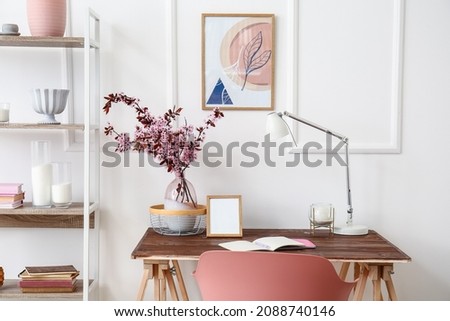 Modern workplace with vase and blossoming branches near light wall