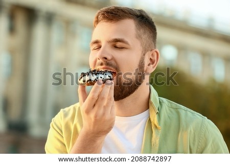 Handsome young man eating sweet donut outdoors Royalty-Free Stock Photo #2088742897