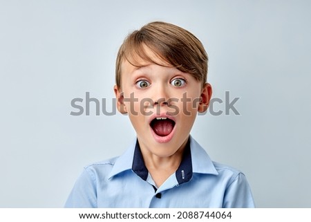 caucasian little boy amazed by news with opened mouth isolated gray color background. Cute young boy in shock, looking at camera in disbelief. Shock, amazement, surprise concept.