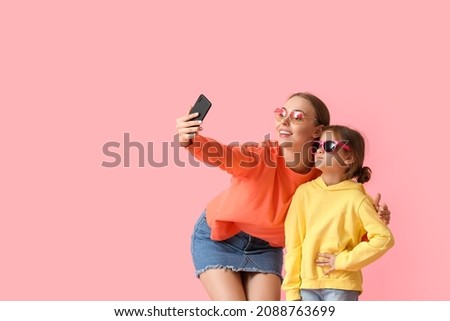 Young woman and her little daughter taking selfie on color background