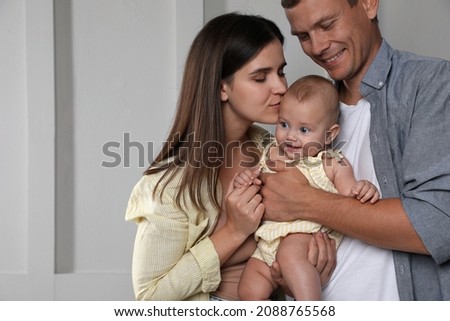 Happy family. Couple with their cute baby near light wall