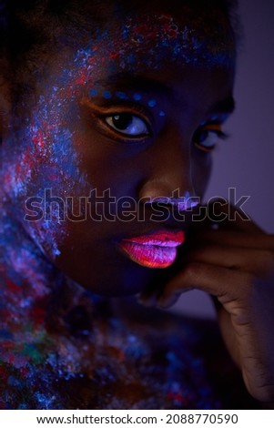 black woman with body art glowing in ultraviolet light. Portrait of beautiful woman painted in fluorescent powder. isolated dark space. beauty, fashion, art, creative shoot concept