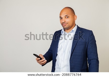 A young African American man is using a smartphone with a confident expression on his face. African American looks at phone screen, reads news in message with mobile social network device.