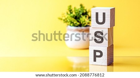 motivational words: USP in 3d wooden alphabet letters on a bright yellow background with copy space, business concept. front view , flower in the background, USP - short for Unique Selling Proposition