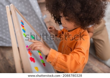 High angle view of african american child playing with signs on magnetic board near mom at home