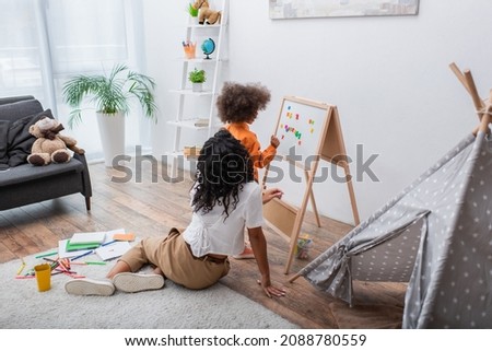 African american girl standing near magnetic board, mother and teepee at home