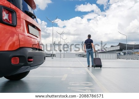 Young man with a suitcase in his hands in the car parking. Back view.