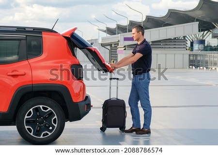 Young man near car with luggage closes tailgate in parking.