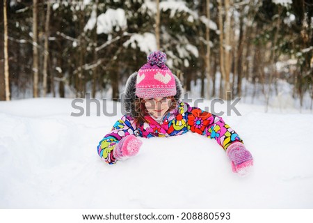Beauty little girl in colorful hat and jacket has fun outdoors in deep snow on perfect winter day 