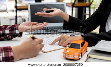 The renter is signing a car rental agreement with the car rental company. After discussing the details and charges with the employee, the employee hand over the car keys to the renter. Royalty-Free Stock Photo #2088807250