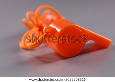 Orange plastic whistle with rope on gray background
