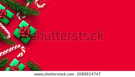 Red and white striped candy cane sticks with fir branches and gift boxes. Red background. Space for text. Vector illustration.
