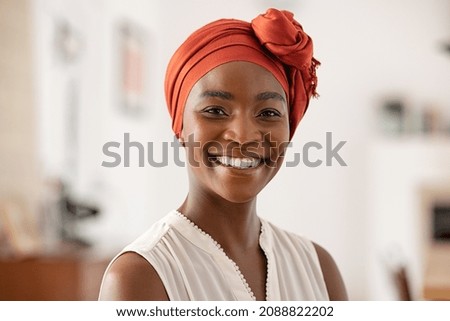 Portrait of smiling middle aged African american woman with headscarf at home. Mid adult black woman with turban looking at camera. Happy mid mature lady wearing traditional african scarf on head. Royalty-Free Stock Photo #2088822202
