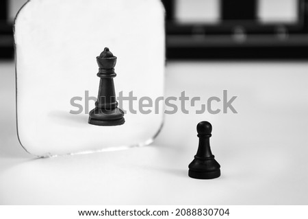 black chess pawn stands in front of the mirror, seeing reflection of queen. concept of career and personal growth, aspiration, improvement, self-confidence. pawn that would be king. Royalty-Free Stock Photo #2088830704