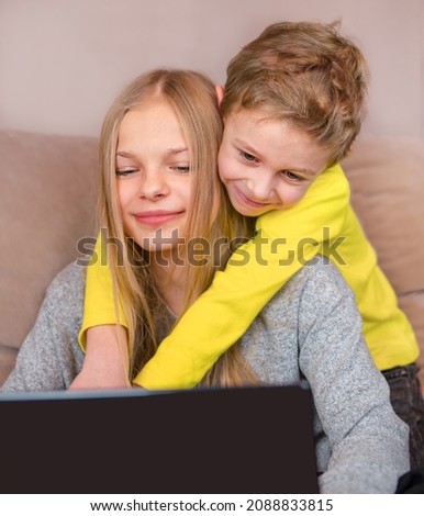 Children communicate on a laptop online. The boy hugs the girl and smiles. Online communication concept