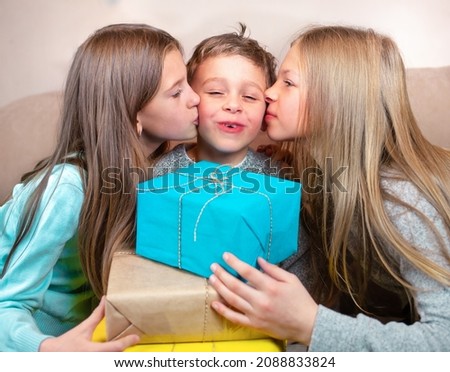 Sisters congratulate their brother Two girls congratulate the boy on his birthday. Girls give the boy gifts and kiss him