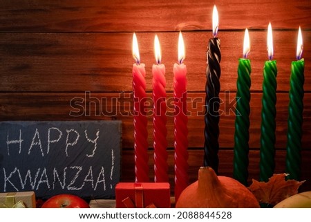 Kwanzaa African American holiday. Seven candles red, black and green on a natural wooden background. Congratulatory inscription and gifts. Symbols of African heritage.