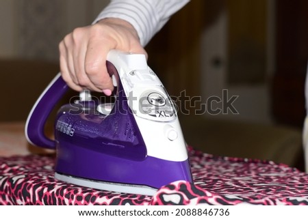 Woman's hand, clothes and iron with which clothes are ironed on an ironing board.
