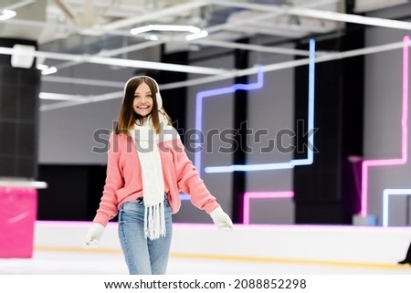 happy woman in ear muffs and pink sweater on ice rink