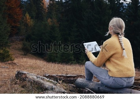 Young woman drawing with graphic tablet near forest in autumn