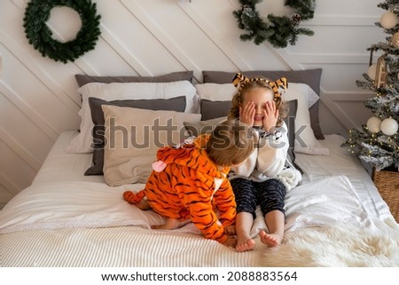 A boy and a girl in tiger cubs costumes play on the bed.Brother and sister in pajamas hugging in bed.The symbol of the new year is a tiger.Children in kigurumi pajamas
