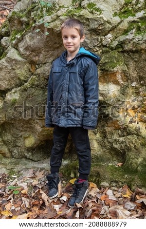 Portrait of boy next to the rock in the forest smiling to the camera. 