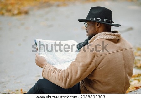 Black man sitting on a road and holding a camera and a map