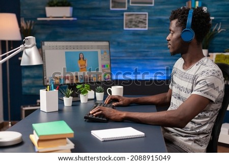 African american man editor with headphones doing photo retouch on computer using creativity post production software. Photographer editing photography sitting at desk in retouching home studio