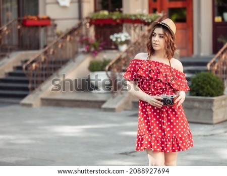 Beautiful women in red polka dot dress and hat with retro camera in the city