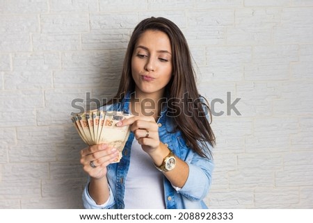 Lovely beautiful girl is holding a large amount of cash, a lot of money from Brazil. Business, income, loan, pay, buy, wealth concept. Royalty-Free Stock Photo #2088928333