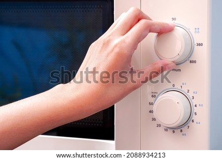 Woman's hand adjusts the temperature with a circular button to warm food from the kitchen microwave.                           Royalty-Free Stock Photo #2088934213