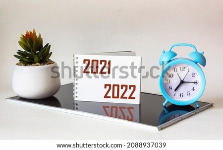 2021-2022. Handwriting of the inscription in a white notepad, on a black and white background, design decision. Nearby a clock and a cactus
