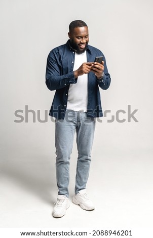 Joyful and carefree African-American man using smartphone isolated on grey, black guy spends leisure in social networks, chatting online, shopping, using new mobile app, full length, vertical Royalty-Free Stock Photo #2088946201