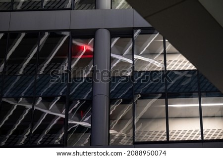 Industrial building front with windows, reflections and red illuminated sign inside.