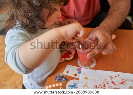 Child rinses paintbrush in glass of water. Art and preschool session