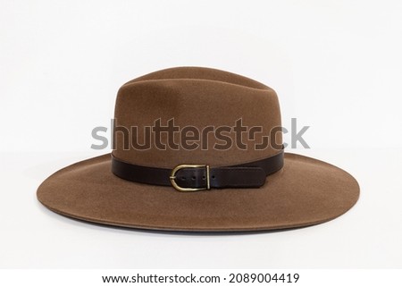 Classic cowboy brown felt hat with strap and copper closure on white background. Side view Royalty-Free Stock Photo #2089004419