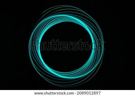 TEAL COLORED NEON CIRCULAR ABSTRACT LIGHT TRAILS ON A BLACK BACKGROUND