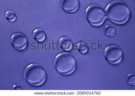 Cosmetic hydrating product or ingredient concept. Glowing blue drops of transparent liquid on a very peri background. Drops gel or oil close up. Abstract dark backdrop. Royalty-Free Stock Photo #2089014760