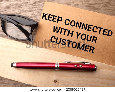 Glasses and pen with text KEEP CONNECTED WITH YOUR CUSTOMER on a wooden background.