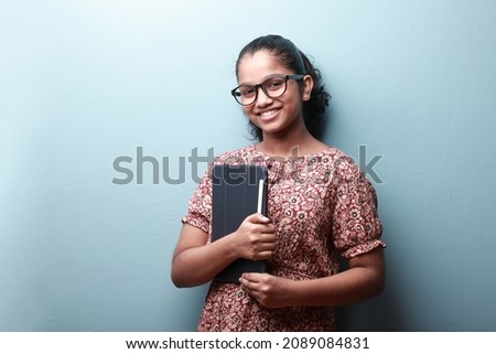 Portrait of a smiling girl of Indian ethnicity holding a tablet phone in hand  Royalty-Free Stock Photo #2089084831